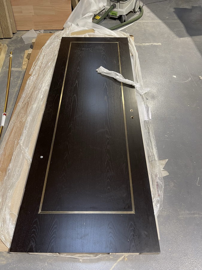 A black stained oak door with a brass inlay border