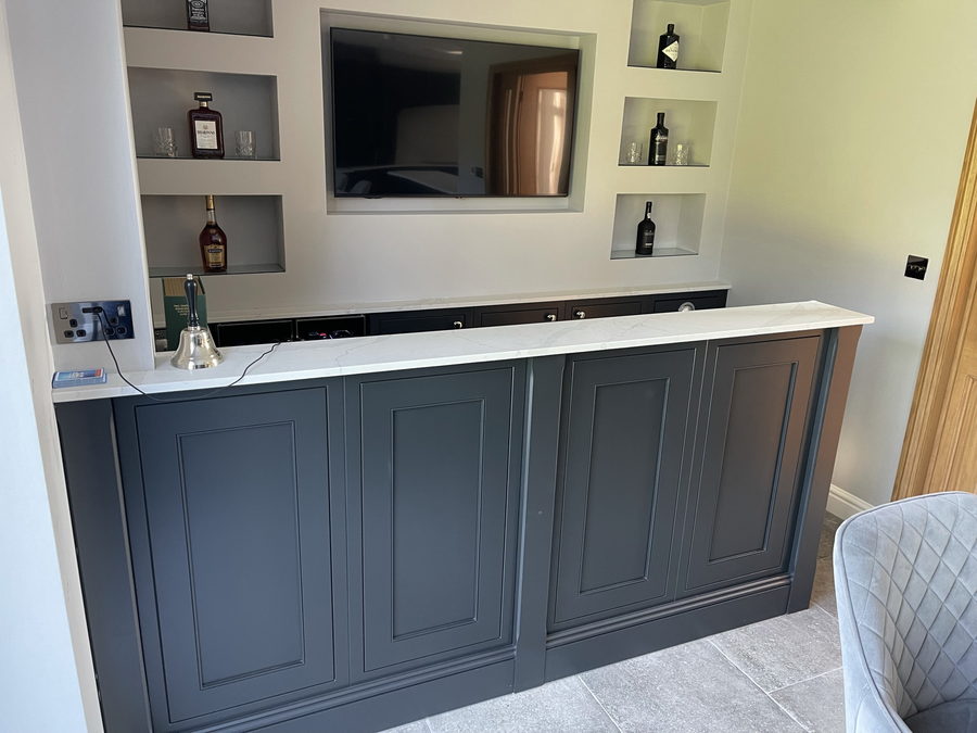 A panelled home bar with a recessed television and stepped bottle niches