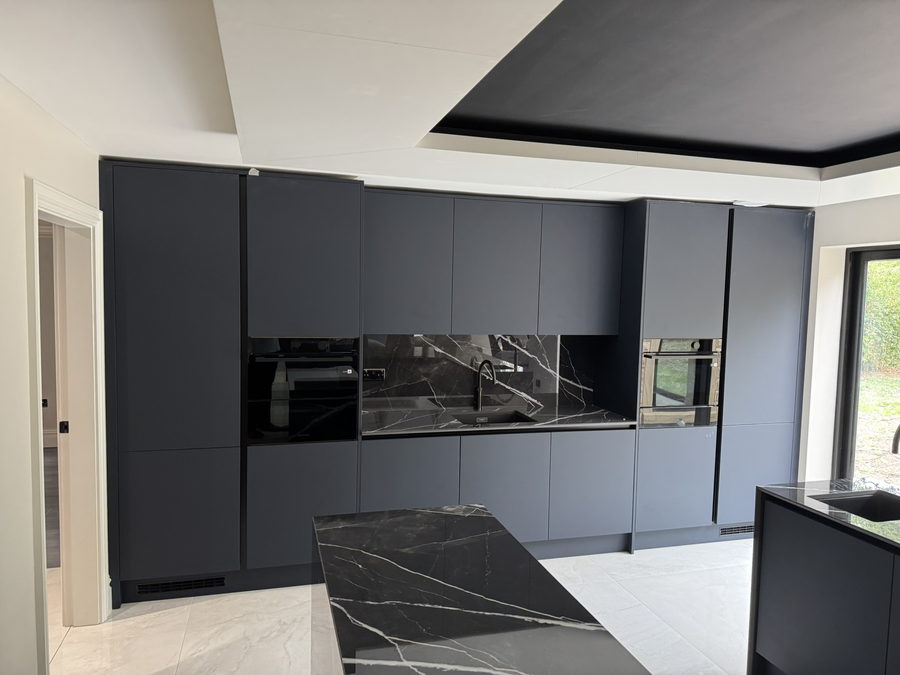 Indigo blue handleless doors with a dark stone splashback and tall ovens