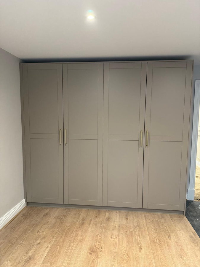 Floor-to-ceiling greige wardrobes with brass handles on an oak floor