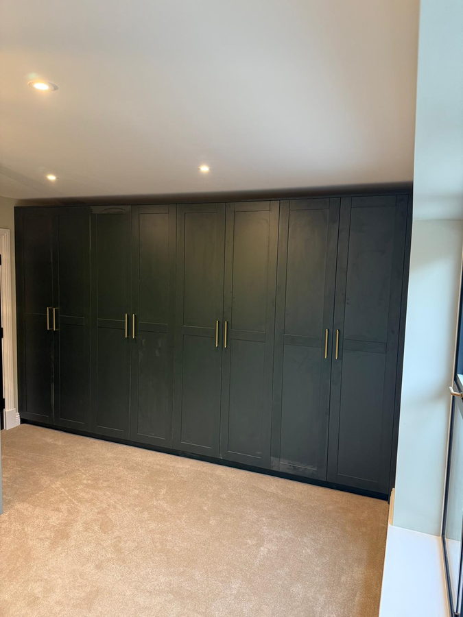 A full wall of dark green shaker wardrobes