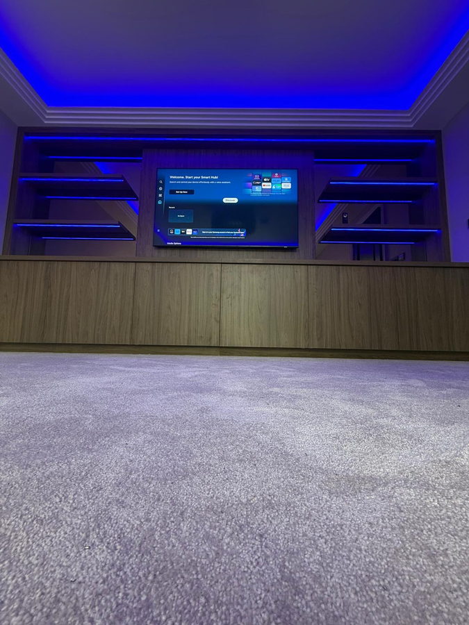 A dark veneer wall with a recessed television, floating shelves and cove lighting