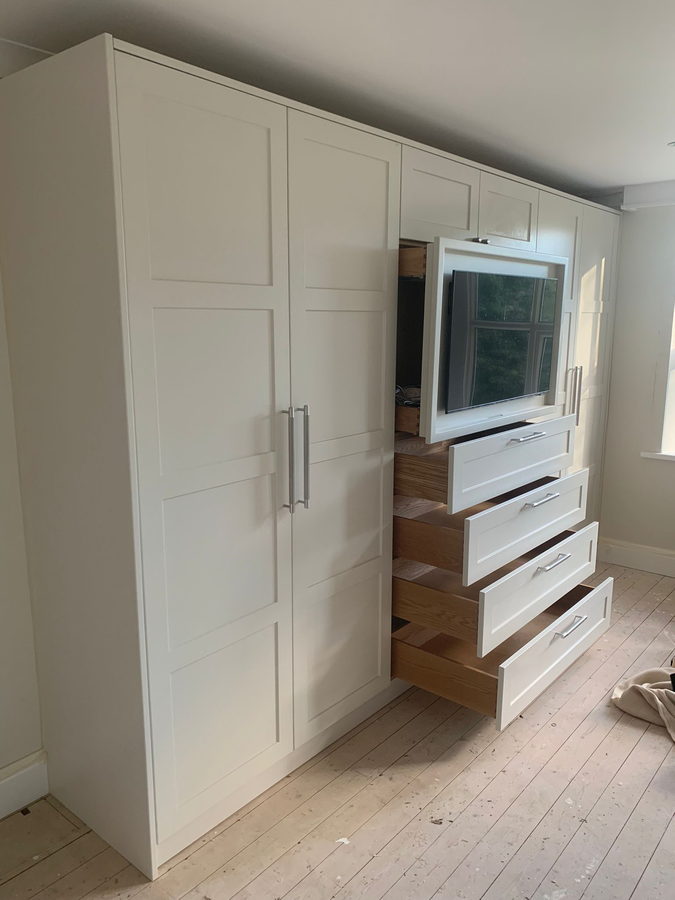 White shaker wardrobes worked around a sloping ceiling, with an open oak drawer bank