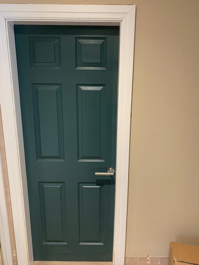 A dark green six-panel door hung in a white lined frame