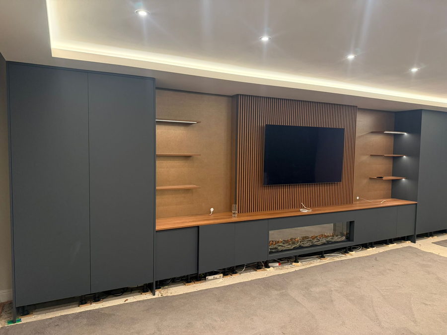 A charcoal wall with an oak slat television panel, floating shelf and ribbon fire