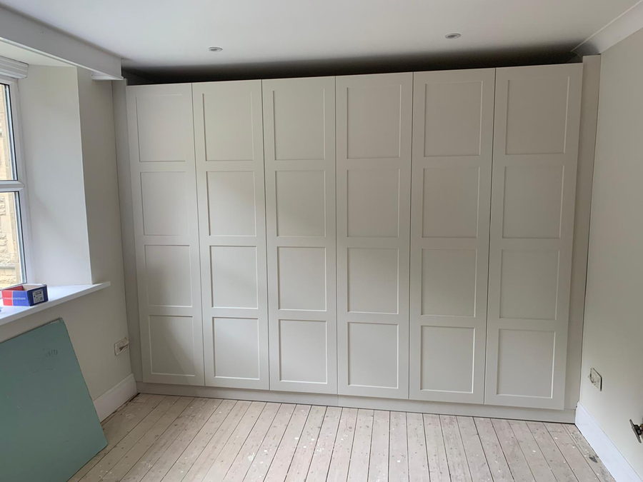 A whole wall of panelled wardrobes with a window seat between