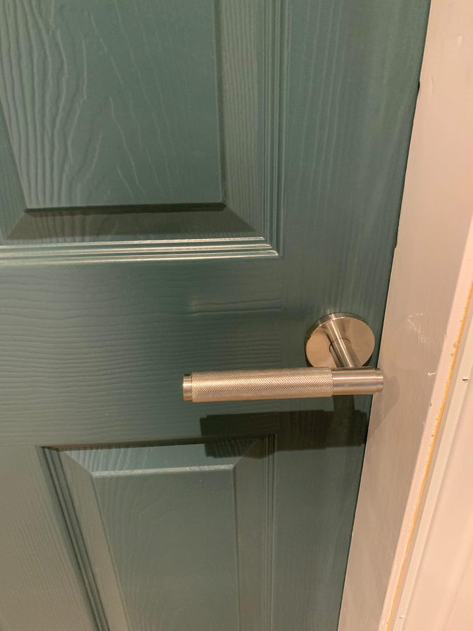 A brushed brass lever on a sage green door