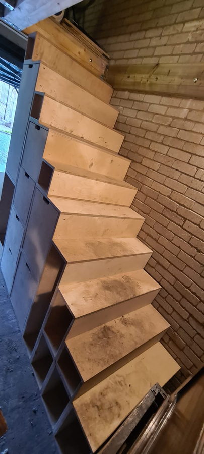 Open oak treads and storage cubbies against an exposed brick stairwell