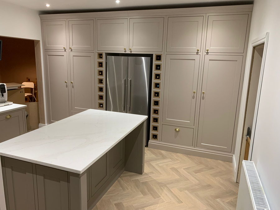 A taupe in-frame kitchen with a quartz island over a herringbone oak floor