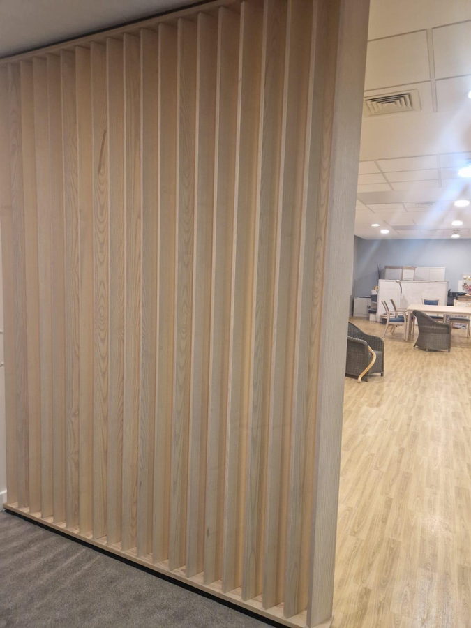A floor-to-ceiling oak slatted divider in an open-plan kitchen