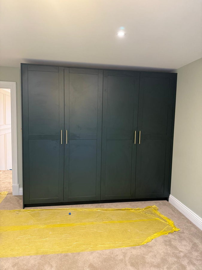A dark green four-door wardrobe with slim brass bar handles